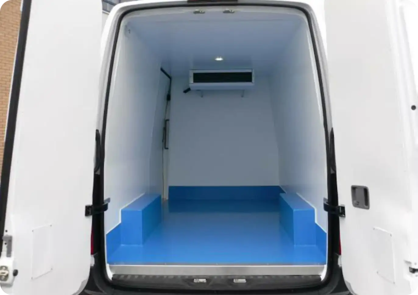 Interior of a freezer truck with a ceiling-mounted cooling unit, white insulated walls, and a blue non-slip floor.