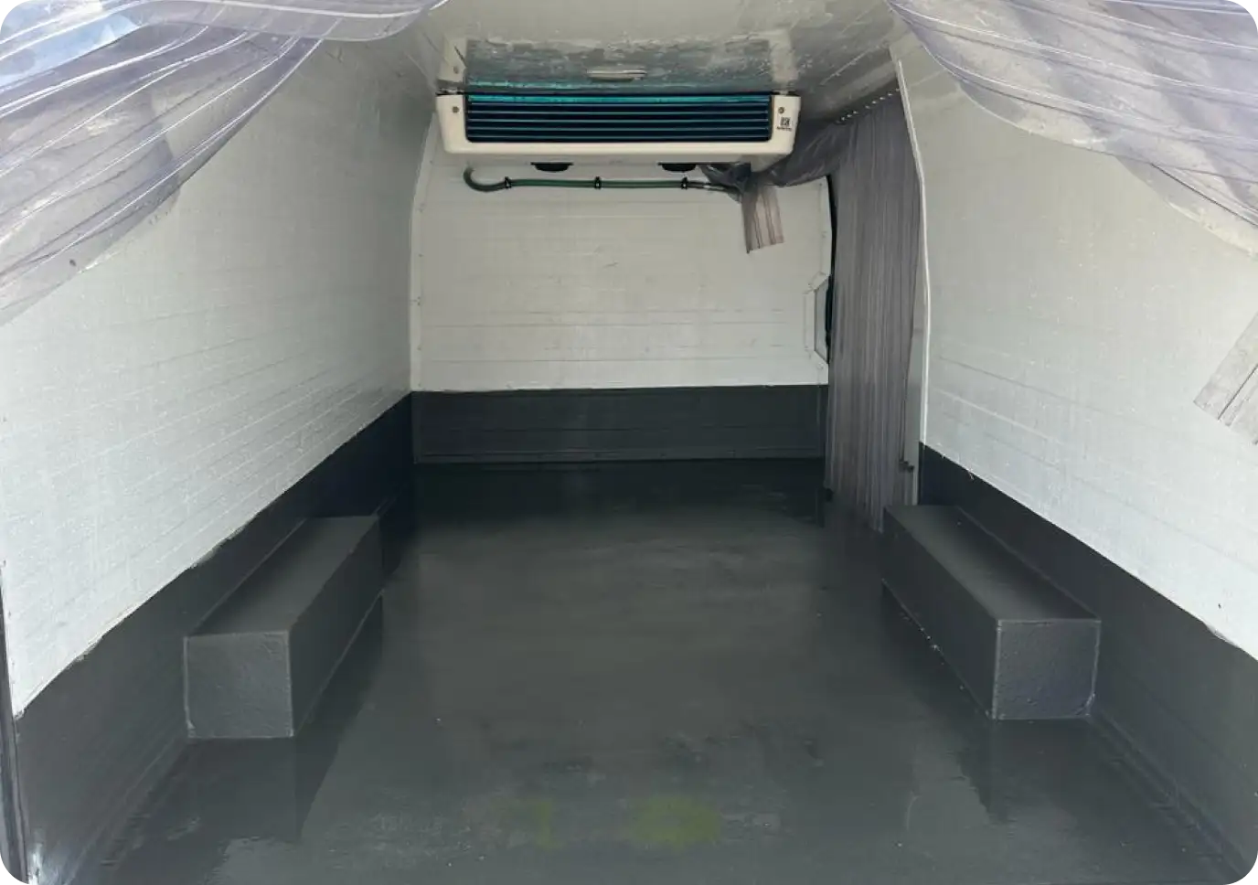 Interior of an insulated freezer van with a cooling unit installed on the ceiling and clean, reflective flooring.