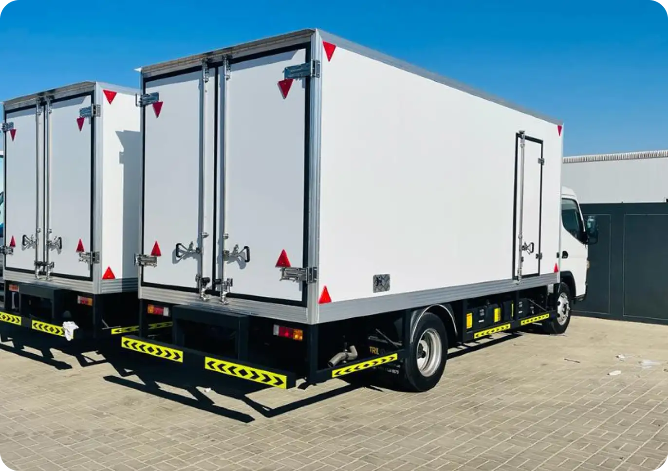 Refrigerated delivery truck with white insulated cargo space, parked in an outdoor lot under a clear blue sky.